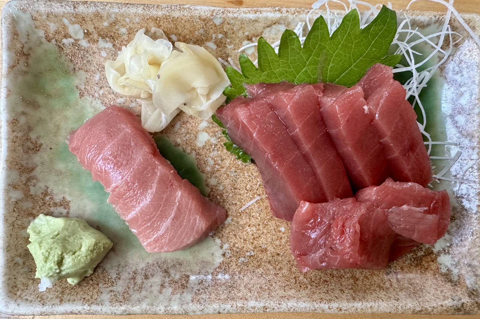 Sashimi arranged on a ceramic plate with shiso, daikon, ginger, and wasabi