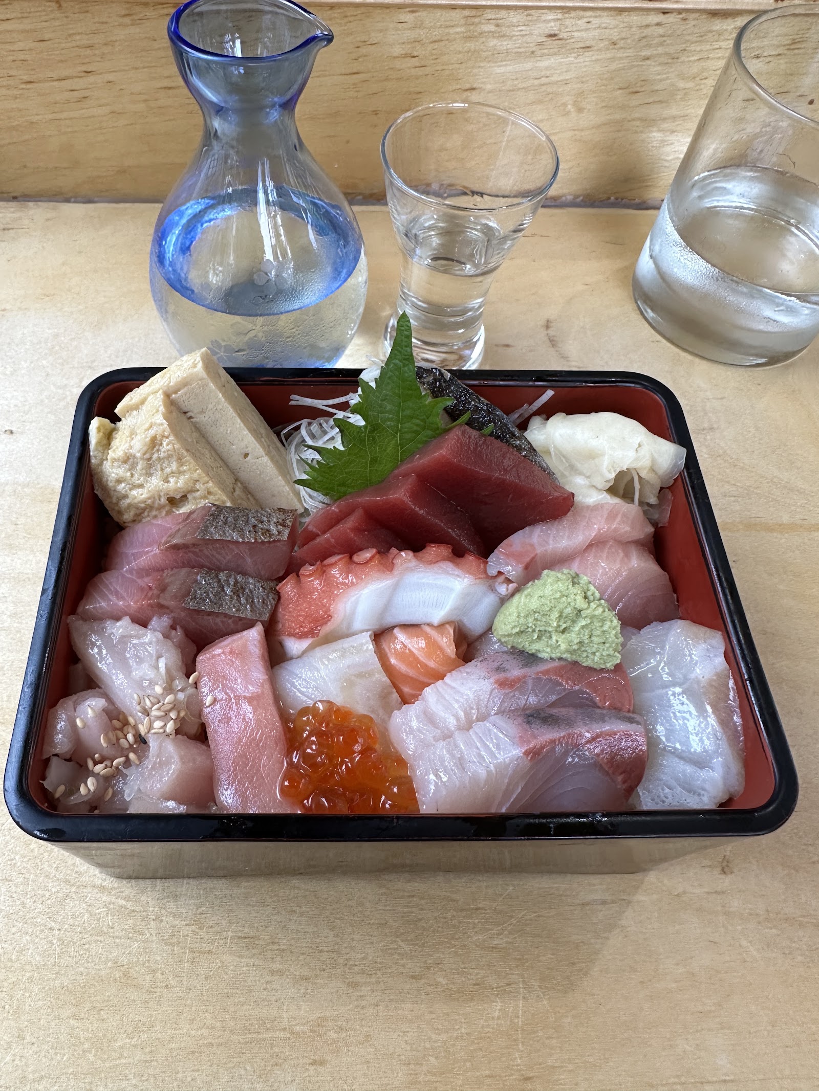Assorted sashimi in a lacquer tray with wasabi, roe, shiso, and glassware